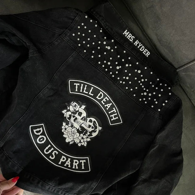 Black studded jacket with text and design, held by a person outdoors.