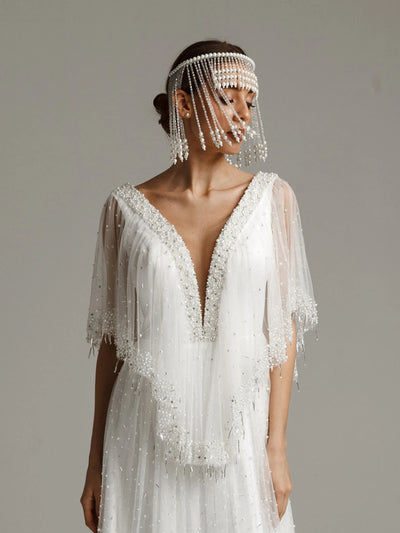 Woman wearing a white beaded wedding dress with a matching headpiece against a neutral background
