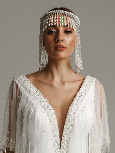 Woman wearing a white beaded headpiece and dress against a neutral background