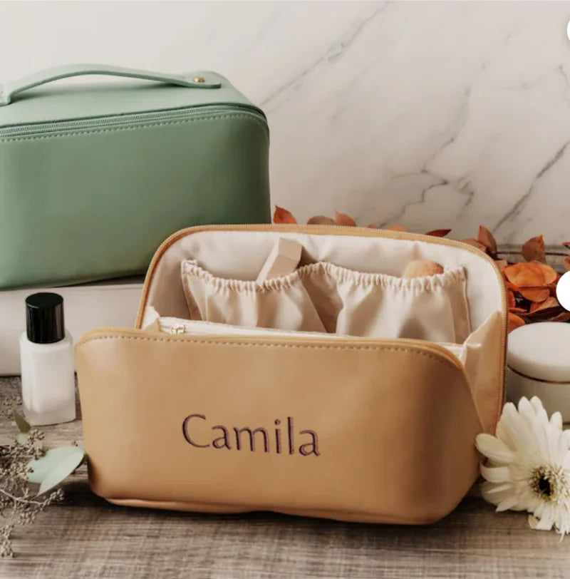 Beige cosmetic bag with 'Camila' branding on a marble surface with a green bag and white flower in the background.