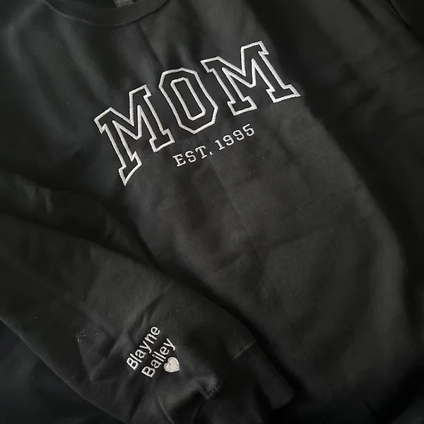Black sweatshirt with 'MOM EST. 1995' text on a dark background