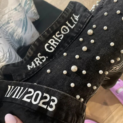 Black denim jacket with 'MRS. GRISOLIA' and '11/11/2023' text, studded with pearls.