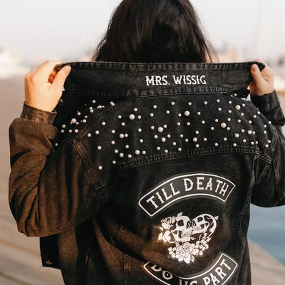 Black studded jacket with text and design, held by a person outdoors.