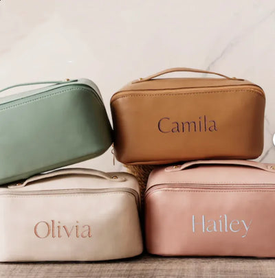 Four cosmetic bags in green, brown, beige, and pink with names engraved on them.