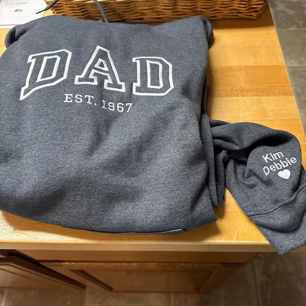 Gray sweatshirt with 'DAD EST. 1967' text on a wooden surface