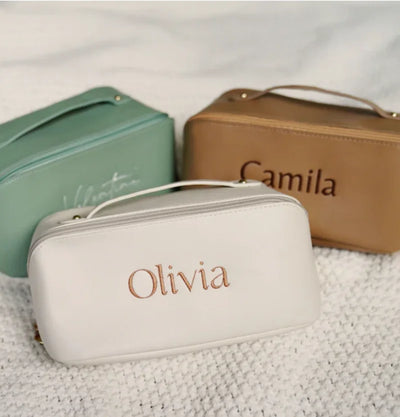 Three cosmetic bags with 'Olivia', 'Camila', and another name partially visible on a textured surface.