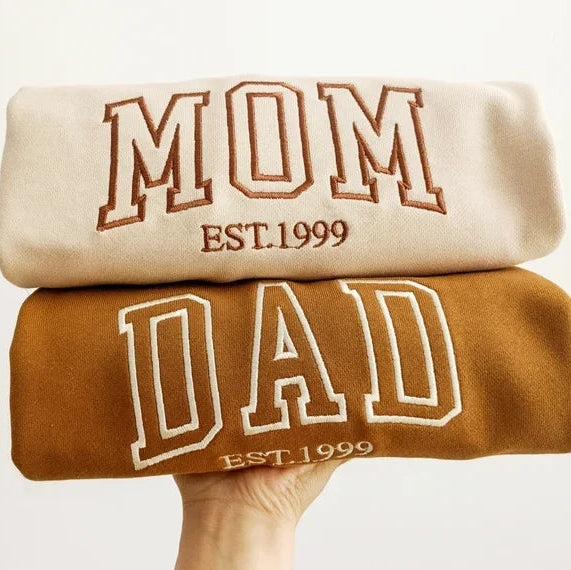 Two sweatshirts stacked on top of each other with 'Mom' and 'Dad' text.