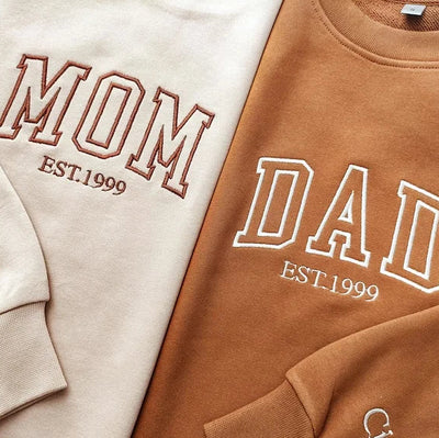 Two sweatshirts with 'MOM EST. 1999', 'DAD EST. 1999', and 'Cici' text on a neutral background.