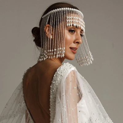 Woman wearing a beaded headpiece and white bridal gown against a neutral background