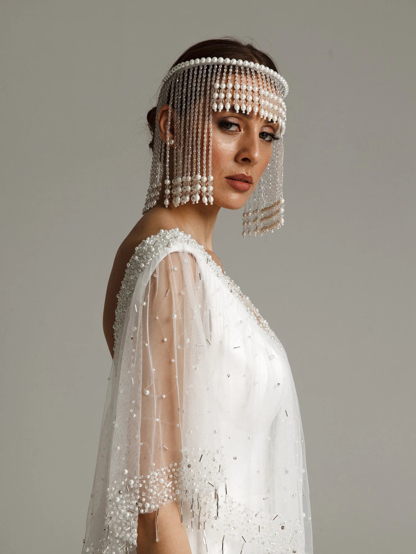 Woman wearing a decorative headpiece with pearls and a matching veil against a neutral background